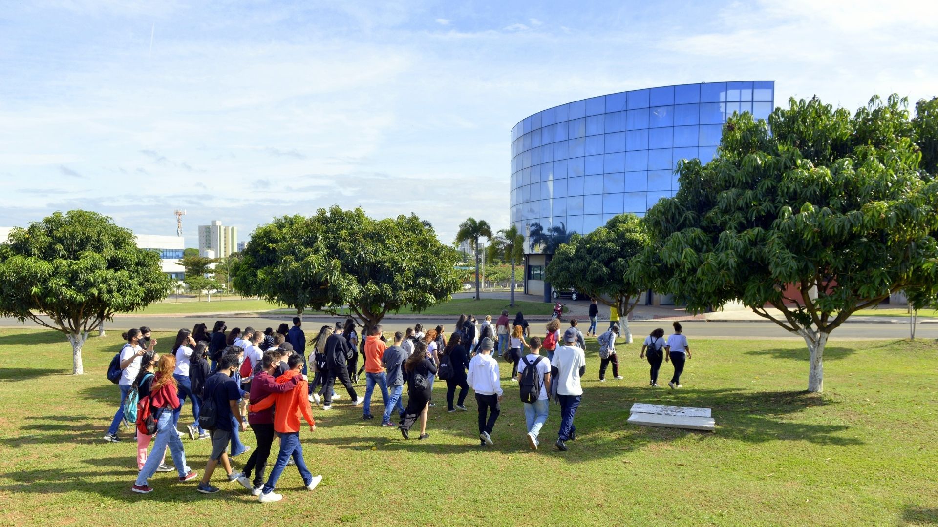 A imagem mostra um grupo de alunos andando em direção ao prédio espelhado da UniMAX, no início das visitas monitoradas.